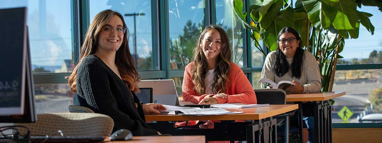 Three students standing sitting at tables and smiling